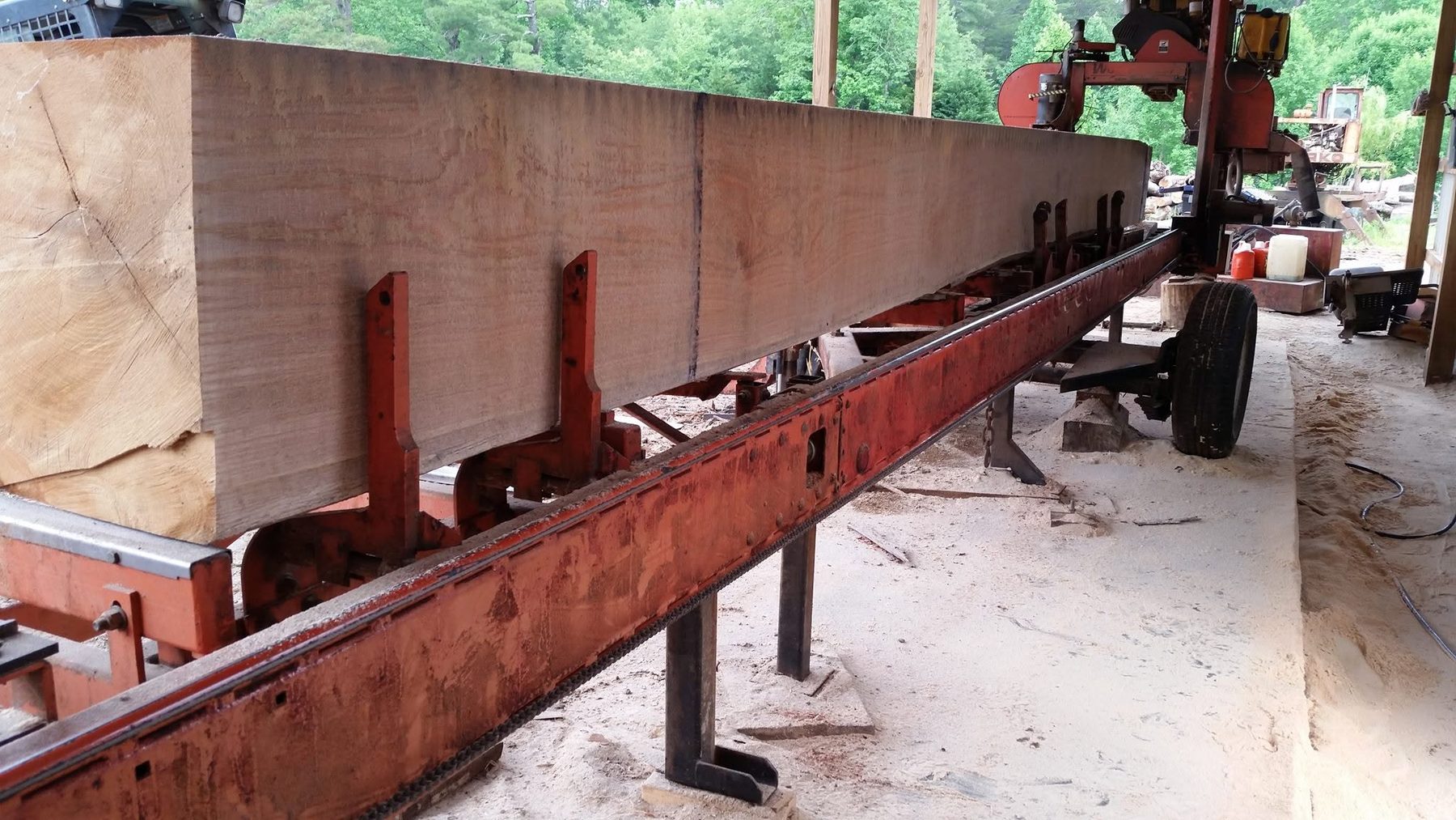 A long, heavy squared beam on the bed of the WoodStar sawmill, sawdust on the ground below