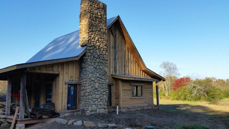 A board-and-batten cabin with a tall river-rock chimney and a metal roof. Opens larger.