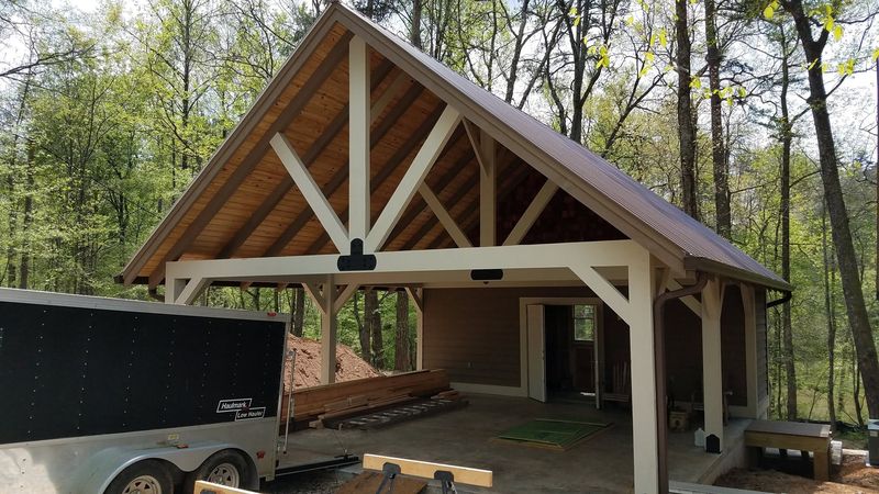 A carport and storage building with a white-painted timber truss in its open gable. Opens larger.