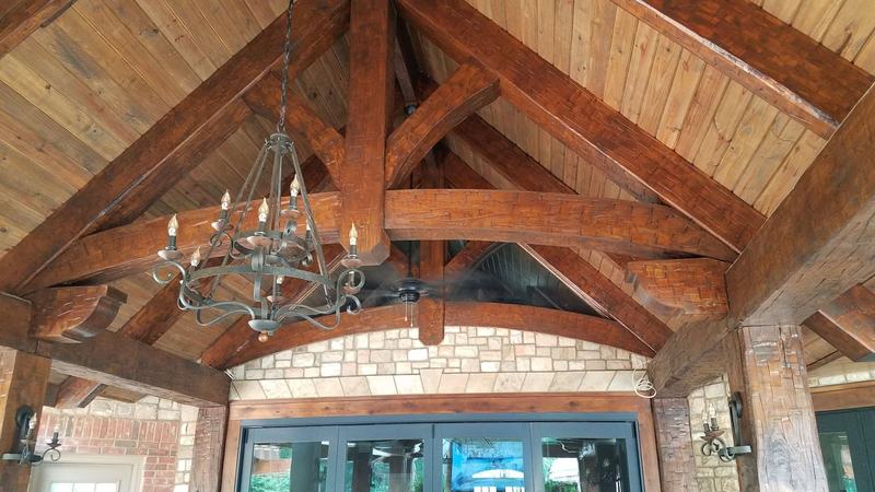 Dark timber trusses and an iron chandelier over a great room with a stone arch and tall windows. Opens larger.