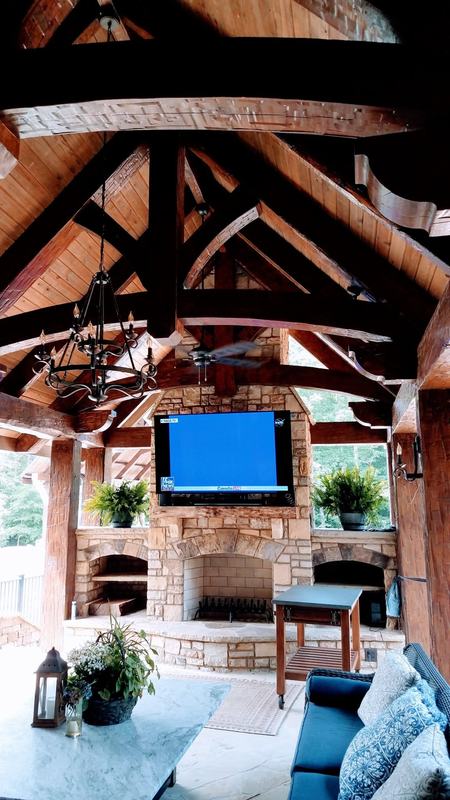 A covered outdoor room with dark timber trusses over a stone fireplace