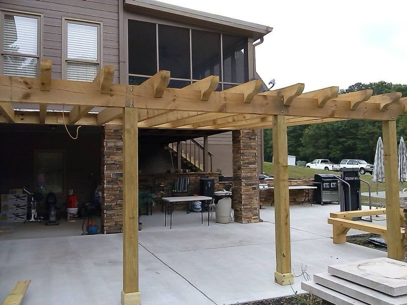 A new timber pergola over a concrete patio beside a house. Opens larger.