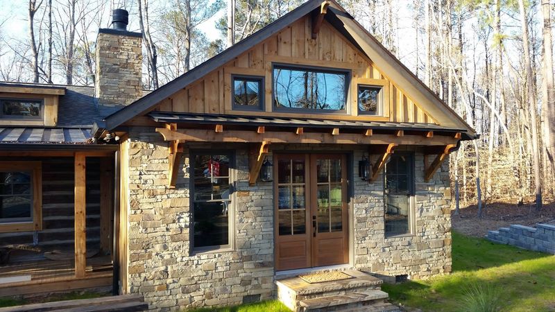 A stone cottage with a board-and-batten gable and heavy timber brackets over the front doors. Opens larger.