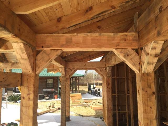Looking up into a timber porch: heavy rough-sawn posts, braces and beams under a plank ceiling. Opens larger.