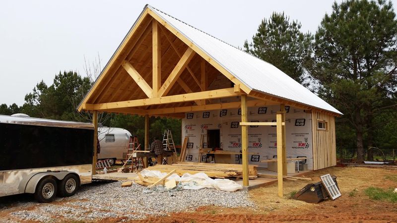A new building with a timber-frame gable porch going up, ladders and lumber on site. Opens larger.